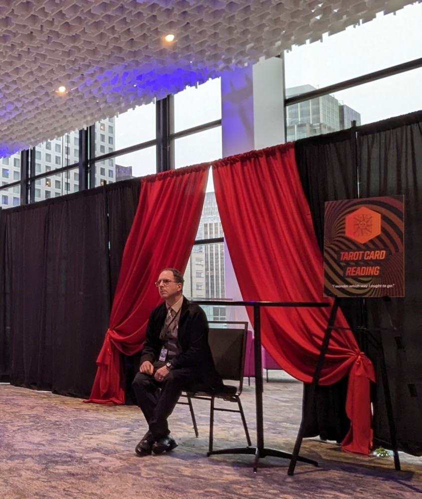 A person sitting on a chair in front of a red and black curtain
Description automatically
generated